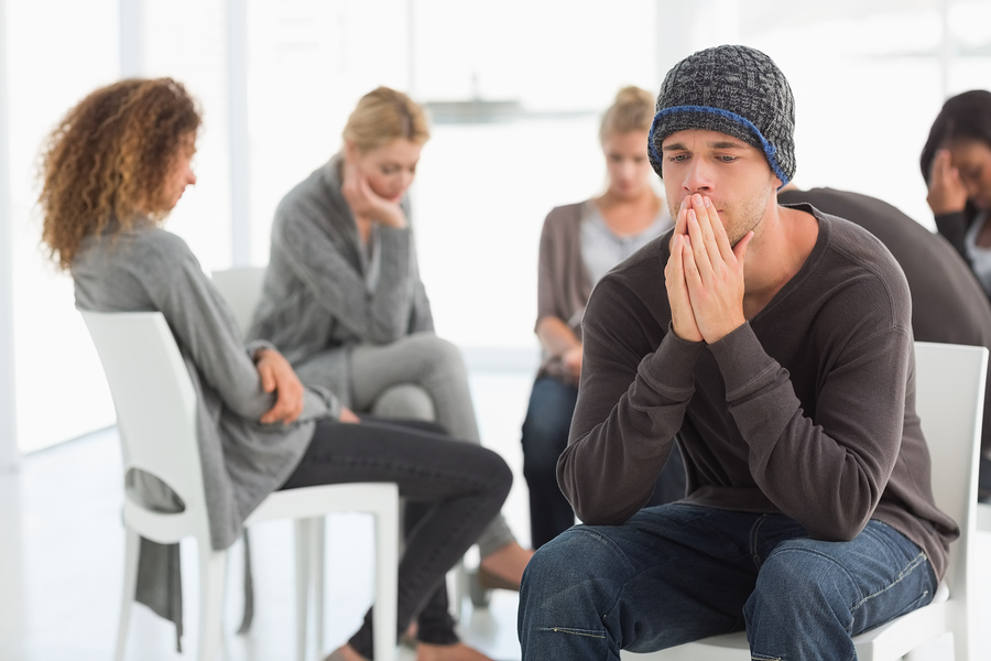 Upset man at rehab group with hands to face at therapy session